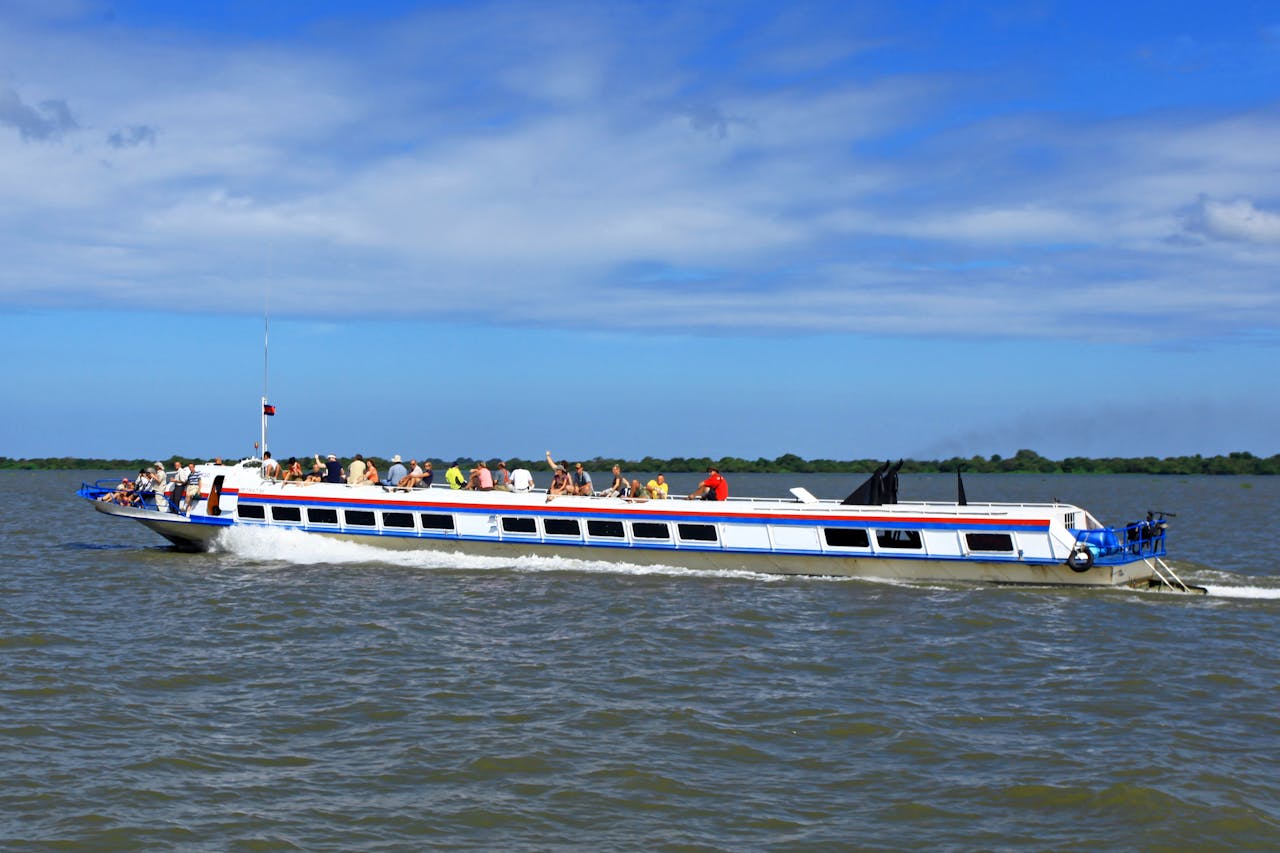 A passenger boat smoothly cruises over open waters on a sunny day, filled with people enjoying the ride.