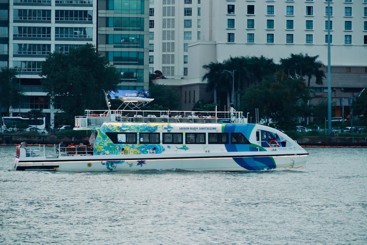 A vibrant sightseeing boat navigates the Saigon River in an urban setting.
